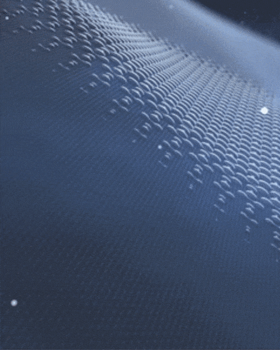 Abstract image of a dark surface with flowing, textured ripples resembling small waves. The surface has a glossy finish, reflecting light and creating a dynamic, fluid-like appearance. The background fades into a smooth gradient.