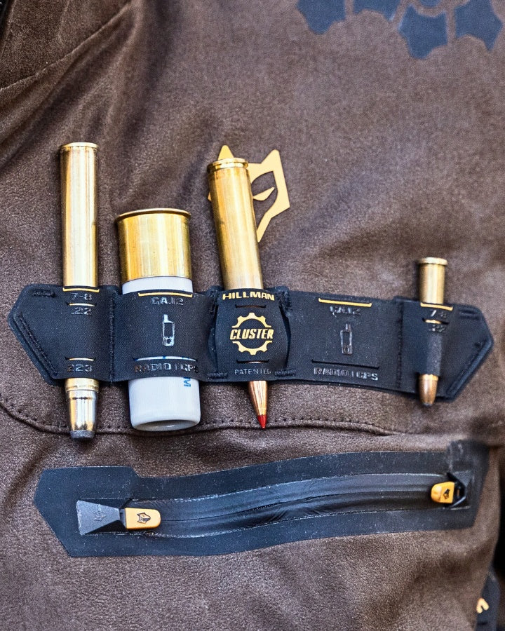 A close-up of a leather belt with four bullet-shaped tools attached. The belt has the text Hillman Cluster and each tool is secured with a small strap. There is a zipped pocket below the belt.