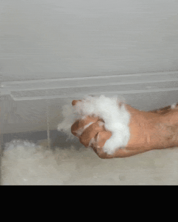 Hand squeezing fluffy white material, resembling insulation or cotton, beneath a rectangular covering.