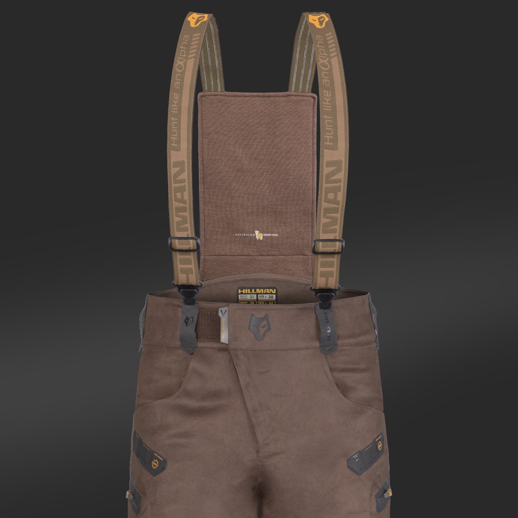The 6OL Matrix Insulated Hunting Trousers by HILLMAN GEAR are waterproof bibs on a black background, designed for extreme cold. They feature olive green suspenders with orange clips and brand logo, black reinforced patches, and multiple pockets.