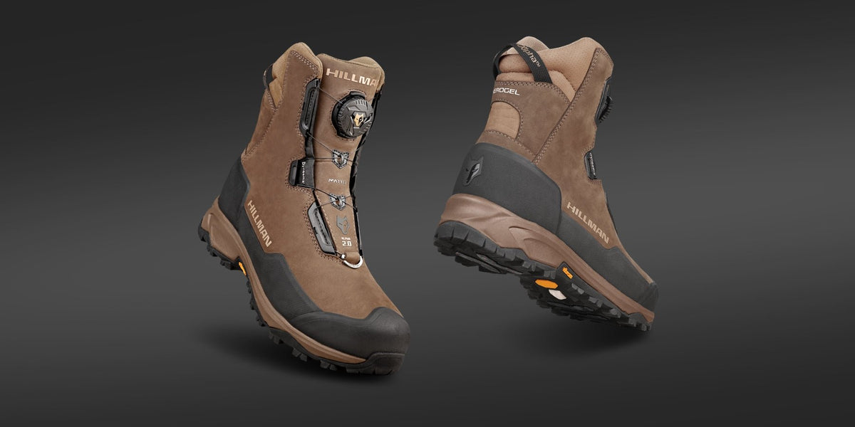 Two rugged brown hiking boots with black soles, reinforced toes, and a dial lacing system, displayed on a dark background. One boot is upright, the other shows the sole and heel.
