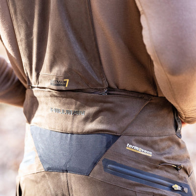 Close-up of a person wearing HILLMAN GEAR insulated hunting trousers waterproof bibs, showing detailed stitching and zippered pockets—ideal outdoor gear for protection and comfort.