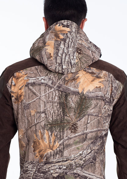 A person wearing the Hillman® Fusion Hunting Jacket 3DX with a hood, featuring a forest pattern of tree bark, branches, leaves, and pine needles. The photo shows the upper back and hood from behind.