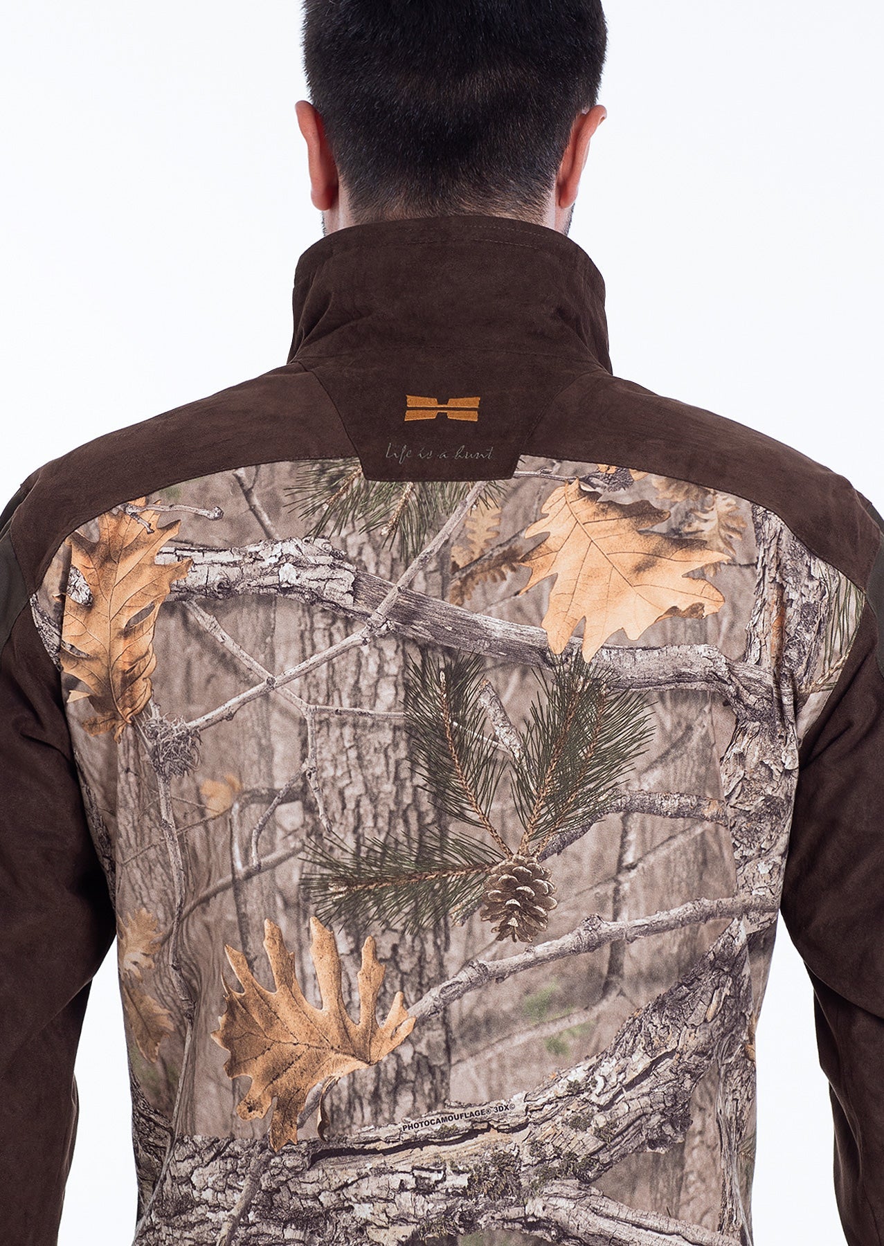 A person seen from behind wearing a Hillman® Fusion Hunting Jacket 3DX, featuring realistic woodland camouflage with tree branches, pine needles, pinecones, and autumn leaves.