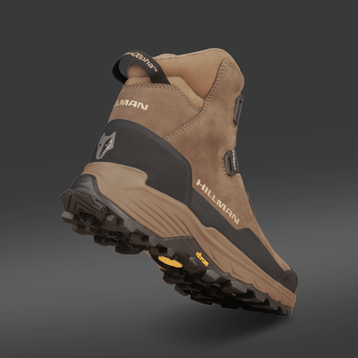 A brown and black HILLMAN PRE-ORDER DRYHUNT 2.0 Waterproof Hunting Boot with rugged tread, HILLMAN branding on the side and heel, is displayed on a dark gradient background, elevating its sole and reinforced heel for performance-focused hunters.