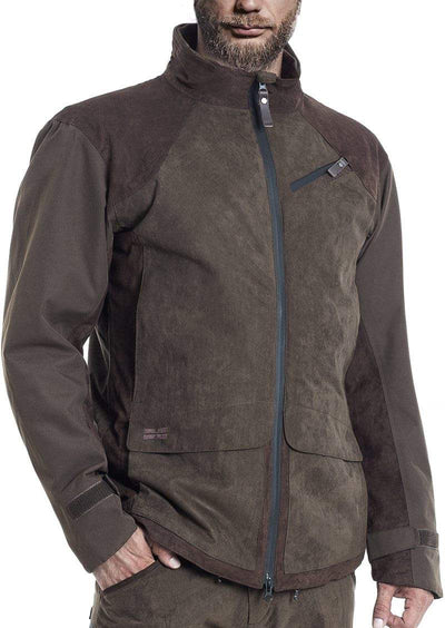A man wears the Hillman® PRE ORDER Fusion Hunting Jacket—brown and dark olive green, waterproof Cordura, high collar, zip front, chest pocket, velcro cuffs—with one hand in his pocket and his face partially visible.