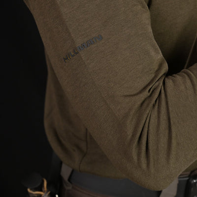 Close-up of a person wearing the HILLMAN bamboo long sleeve hunting t-shirt—an ultralight all-season base layer with moisture control—featuring HILLMAN branding on the sleeve and a belt with knife handle, set against a black background.
